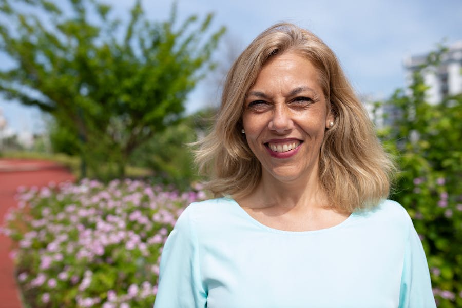 A woman smiling warmly outdoors in a sunny garden
